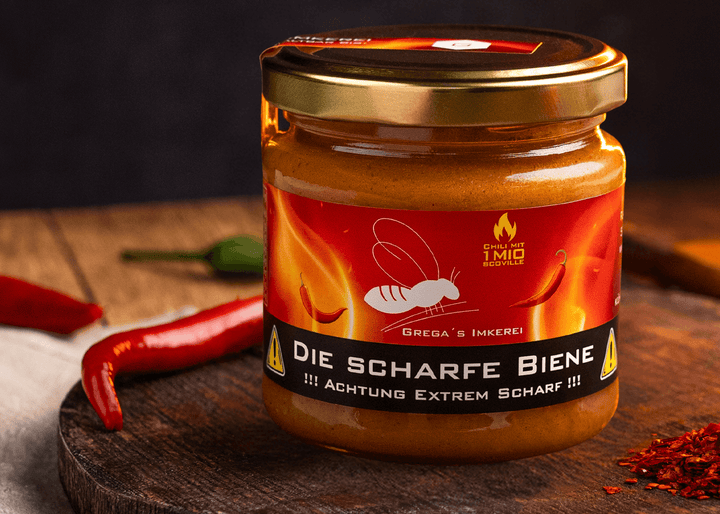 "Nahaufnahme von 'Die Scharfe Biene' Honig neben einer einzelnen Carolina Reaper Chili auf rustikalem Holzuntergrund."
